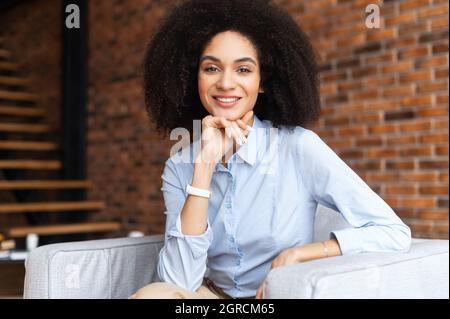 Headshot portrait of a charming elegant biracial woman with her hand on a chin, wearing shirt looking at the camera. Close-up of mixed-race female office worker or a teacher Stock Photo