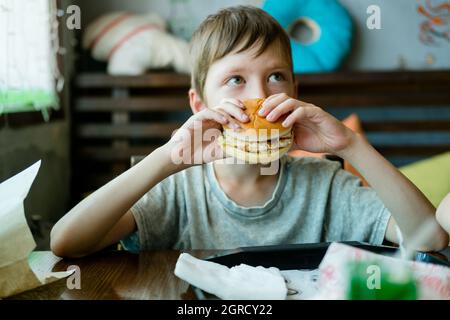 boy eating a big burger with a cutlet. Hamburger in the hands of a child. Delicious and satisfying chicken cutlet burger. Takeout food Stock Photo