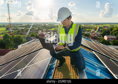 An engineer working at solar panels installed on a roof of a large industrial building or a warehouse. Industrial buildings on rooftop. Stock Photo