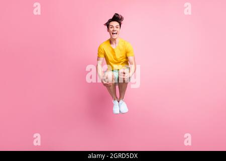 Photo of impressed pretty young guy dressed yellow t-shirt jumping high isolated pink color background Stock Photo