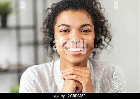 Close-up portrait of smiling intelligent biracial woman in headset and smart casual shirt, mixed-race woman looks at camera and talking online Stock Photo