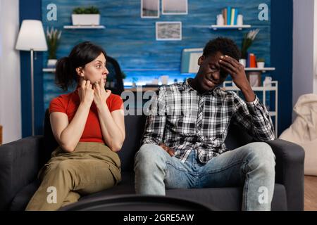 Interracial couple getting into argument sitting on couch. Irritated mixed race partners fighting and having relationship problems. Caucasian woman yelling at african american man Stock Photo