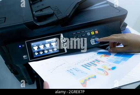 Office worker prints paper on multifunction laser printer. Copy, print, scan, and fax machine in office. Document and paper work. Print technology. Stock Photo