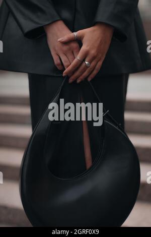 A Female Figure In Black Leather Clothing Holding A Stylish Handbag. Women's Fashion Street Style