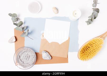 Blank card mockup in kraft envelope among natural organic cosmetics and accessories on white table, top view Stock Photo