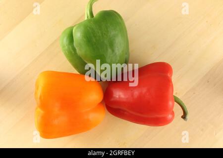 Whole bell peppers in red, orange and green on a pale wood grain  background with copy space Stock Photo