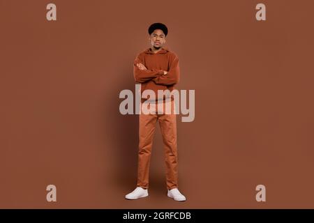 Photo of self-assured successful african guy crossed hands wear sweatshirt pants sneakers isolated on brown background Stock Photo