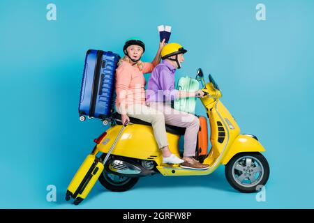 Photo of sweet excited senior husband wife driving motorcycle dressed helmets holding bags tickets isolated blue color background Stock Photo