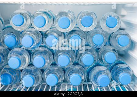 Rows of many transparent plastic bottle with drinking water supply in white refrigerator. Mineral water stack storage in fridge to drink on hot summer Stock Photo