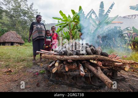 Indonesia, Papua, city of Wamena, members of the Dani tribe perform traditional cooking of sweet potatoes in an earth oven, with stones heated by wood fire and wrapped in plant leaves. Baliem Valley Cultural Festival, every August, tribes come together to perform ancestral war scenes, parade and dance in traditional clothes Stock Photo