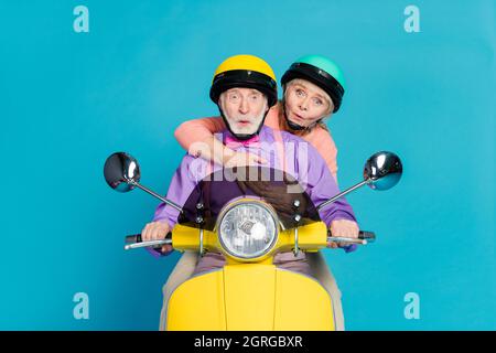 Photo of retired pensioner couple ride bike wear helmet amazed shocked isolated on blue color background Stock Photo