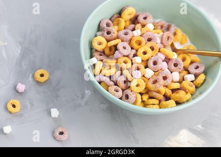 Multi colored cereal fruit loops and milk in a bowl with spoon on gray background. Top view, copy space. Breakfast concept Stock Photo