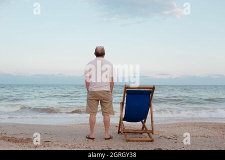 Man admires sky and sea near sun lounger on seashore Stock Photo