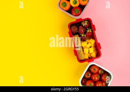 School lunch boxes for storing food and a quick lunch with vegetables and fruits on colored backgrounds. Healthy food and strength. Stock Photo