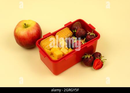 Lunch box with fruits, cookies and cheese for a quick lunch on a colored background. Healthy food. Stock Photo