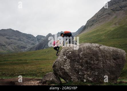 dad helping his daughter climb whilst hiking the Scottish Highlands Stock Photo
