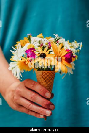 Close up of hand holding a sugar cone full of wildflowers. Stock Photo