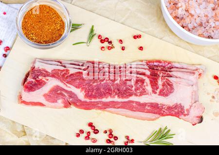 Top view of thin slices of marbled beef with spices, rosemary and salt on light wooden cutting board ready for cooking. Stock Photo