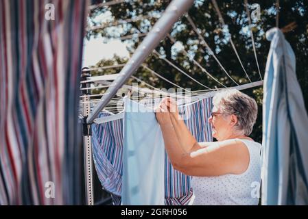 Senior woman hanging laundry on an outdoor clothesline. Stock Photo