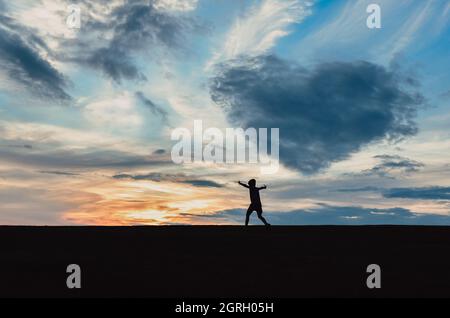 Silhouette of child against sky at sunset with a heart shaped cloud. Stock Photo