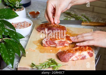 Raw marbled beef steak slices with salt and spices on wooden cutting board background. The preparation of a fresh meat for dinner. Stock Photo
