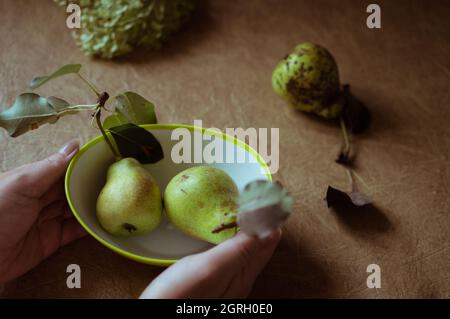 Green pears and a plate in women's hands on a brown background Stock Photo