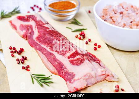 Top view of thin slices of marbled beef with spices, rosemary and salt on light wooden cutting board ready for cooking. Stock Photo