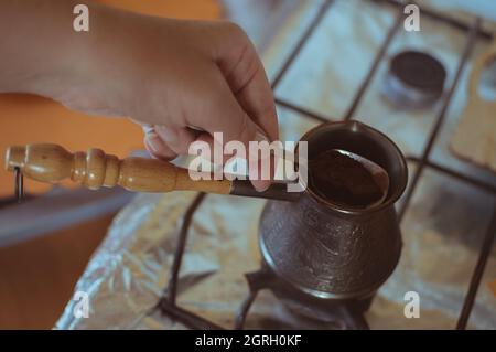Hand pours ground coffee into Turkish coffee pot Stock Photo