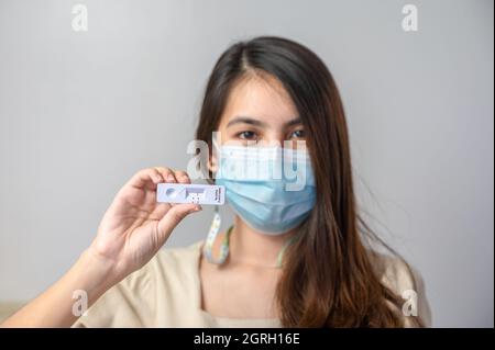 Asian woman wearing face mask showing negative result of rapid antigen test kit of home use. No infection of Covid-19, Coronavirus Stock Photo