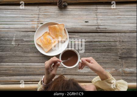 Female hand stirring hot cocoa drink in white cup on bamboo table in the morning. Top view Stock Photo
