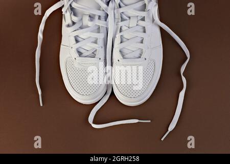 Top view of white stylish sneakers with untied laces on a brown background. Stock Photo