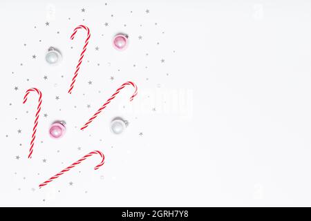 Christmas flat lay. Christmas candy canes, pink and silver balls, silver glitter confetti stars on white background. Flat design, top view, copy space. Stock Photo