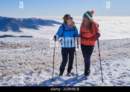 Two women hikers enjoying themselves up in the Leaota mountains (part of Carpathians), Romania, with a sea of clouds behind them. Winter, hiking, adve Stock Photo