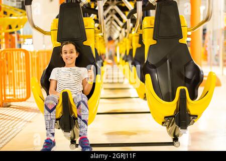 Girl on a thrilling roller coaster ride at an amusement park with arms raised and yelling with excitement Stock Photo