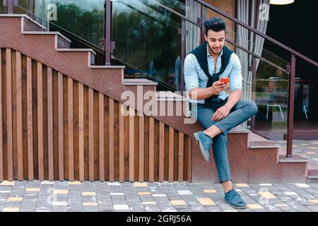 Attractive young Arabic man standing with suitcase in hand and posing for on camera, put one foot before the other and is based on the stairs near the Stock Photo