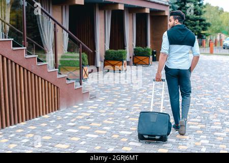 Young Guy Arab Businessman Student Came go to Restaurant With Suitcase in Hand, Smiling at Camera, Stops and Looks Away. Stock Photo