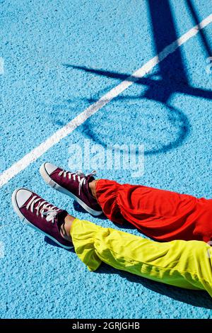 closeup of a man, wearing a colorful clown costume, lying face up on an outdoor basketball court Stock Photo
