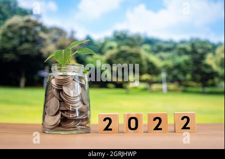 Glass bottles full of coins, and wooden cubes with 2022 text Stock Photo