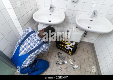 Plumber Fixing Pipe In Bathroom. Plumbing Maintenance In Bathroom Stock Photo