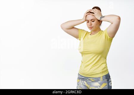 Image of young plus size girl workout in gym, doing fitness, holding hands on head, looking tired of exercises, white background Stock Photo