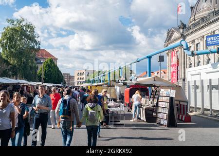 Berlin, Germany - August 28 2017; Blue overhead ground water pipes above people and crafts for sale in city street markets in afternoon shade with cat Stock Photo