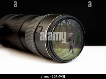 Digital zoom lens showing a young girl walking alone in the park through the lens. Concept someone may be watching Stock Photo