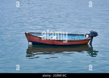 Small wooden fishing boat with one outboard motor in clear blue water. Stock Photo