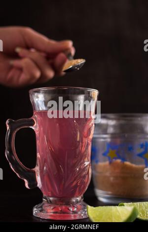 Hand stirring the sugar in a tea cup on a black table with a green sliced lemon and a sugar pot Stock Photo