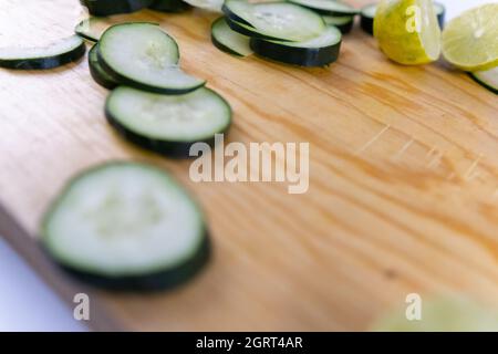 Fresh cucumber slices and a lime cut in half on wooden cutting board Stock Photo