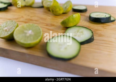 Fresh cucumber slices and halved limes on wooden cutting board Stock Photo
