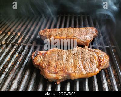 Beef sirloin steaks cooking on a barbeque grill Stock Photo