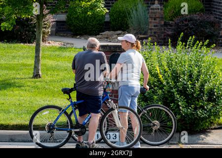 A senior Caucasian man stops his bicycle in the street of a residential neighborhood to answer his mobile phone while a woman companion waits. USA. Stock Photo
