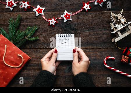 Christmas shopping list. Christmas Shopping on Budget. Christmas Money Saving Tips. Female hands with small notepad and text shopping list Stock Photo
