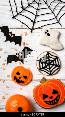 Halloween food and decorations, vertical top view. Halloween cookies, ghost, web and bats, flat lay. Funny objects on white wooden table for Hallowen. Stock Photo